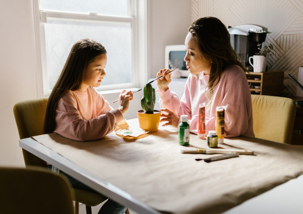 the photo shows a mother and daughter painting an object together.