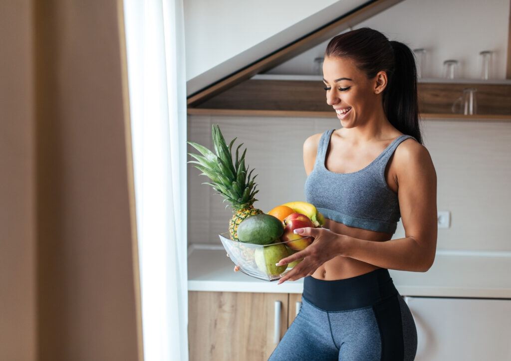 In the photo, a woman dressed in fitness clothes is holding a plate of fruit.